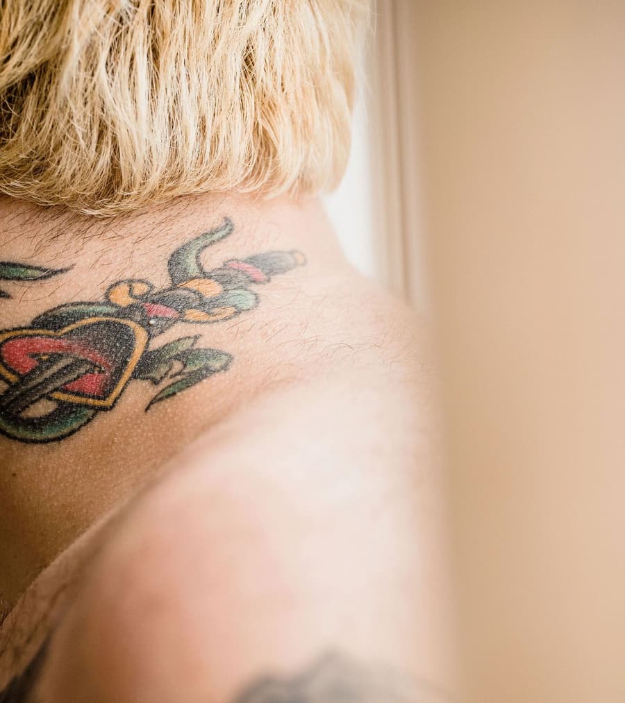 Healed traditional heart pierced by a dagger across the back of a shoulder