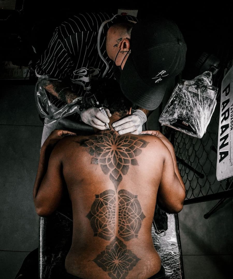 An artist leaning over a client's back, a dotwork lotus piece fresh on the spine