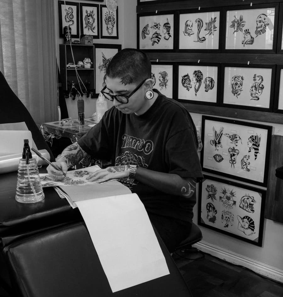 Kit Moreno drawing at a desk under a wall of framed traditional flash