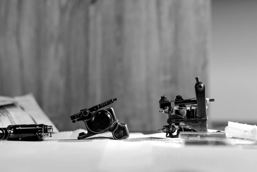 A row of tattoo machines laid out on a bench, in black and white
