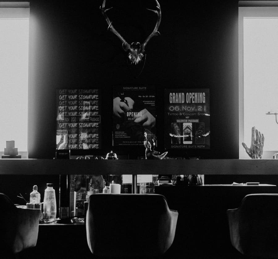 The front room: two black chairs under a stag skull, bottles along the bench, in black and white